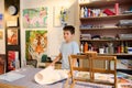 Teenage boy learns drawing in art class, standing at desk against a wall with painted pictures. Fine visual art concept