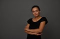 Confident portrait of serene pretty woman of African ethnicity poses with crossed arms on waist, looks at camera isolated against