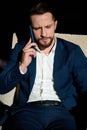 Confident portrait of a young successful businessman in business casual suit talking on mobile phone while sitting on an armchair Royalty Free Stock Photo