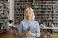 Confident positive Asian blonde college girl standing in university library