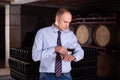 Confident male winemaker degusting red wine in wine cellar near bottles racks Royalty Free Stock Photo