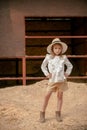 Preteen girl standing akimbo on pile of sawdust near empty barn of country estate