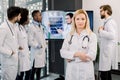 Confident pretty middle aged female doctor posing and the hospital with arms crossed, while her multiracial medical team Royalty Free Stock Photo