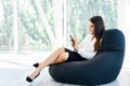 Confident pretty woman using mobile phone answering important messages sitting on bean bag chair