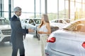 Young female customer asking mature sales manager to help in car dealership. Royalty Free Stock Photo