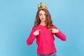 Confident proud woman with wavy hair wearing pink pullover and gold crown, pointing at herself with finger, superior privileged