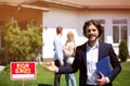 Confident real estate broker and blurred young couple in front of country house, outdoors. Blank space Royalty Free Stock Photo