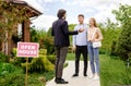 Confident realtor showing house for sale to newlywed young couple, outdoors Royalty Free Stock Photo