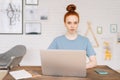 Confident redhead young woman freelancer is working on laptop computer at the desk at home office. Royalty Free Stock Photo