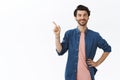 Confident, sassy young bearded gay man in pink t-shirt, shirt, hold hand on waist, pointing upper left corner and