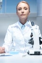 Confident scientist in white coat sitting at workplace in laboratory