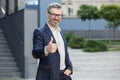 Confident senior businessman giving thumbs up outside modern office building Royalty Free Stock Photo