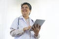 Confident senior female doctor happy using tablet computer standing in clinic. Royalty Free Stock Photo