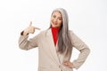 Confident senior woman, businesswoman in suit pointing finger at herself and smiling with self-assured face expression Royalty Free Stock Photo