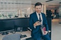 Confident smiling entrepreneur using smartphone and smiling while standing in office Royalty Free Stock Photo