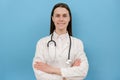 Confident smiling female doctor wear white medical coat, stethoscope look at camera standing on blue color background wall. Happy Royalty Free Stock Photo