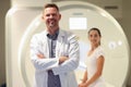 Confident smiling male doctor close-up and female patient and CT scanner in background. Royalty Free Stock Photo