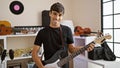 Confident, smiling young hispanic man masters the electric guitar in music studio, portraying an attractive artist excitedly Royalty Free Stock Photo