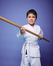 Confident strong concentrated boy - Aikido wrestler in white kimono stands with a wooden jo weapon in his hands. Oriental martial