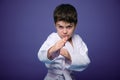 Confident strong kid, aikido fighter practicing martial skills on purple background with advertising copy space. Oriental martial