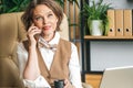 Confident stylish mature middle aged elderly woman in office.Workplace with laptop,using talking by mobile phone.General Royalty Free Stock Photo