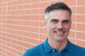 Confident and successful. Cheerful mature man in blue polo shirt looking at camera while standing against brick wall urban Royalty Free Stock Photo