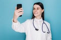 Confident and successful woman doctor or medic taking selfie with smartphone, using mobile app, making video for social network Royalty Free Stock Photo