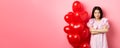 Confident teenage girl cross arms on chest and smile, celebrating valentines day in cute dress with red heart balloons Royalty Free Stock Photo