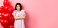 Confident teenage girl cross arms on chest and smile, celebrating valentines day in cute dress with red heart balloons Royalty Free Stock Photo