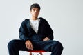 Confident trendy mixed race man sitting on a chair on white background looking to camera