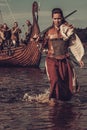 Confident viking woman with sword walking along the shore with Drakkar on the background Royalty Free Stock Photo