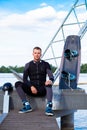 Confident wakeboarder sitting on pier with wakeboard, preparing for training Royalty Free Stock Photo