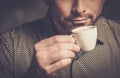 Confident well-groomed bearded man with cup of coffee on dark background.