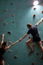 Confident woman and man mountaineers climbing artificial rock wall with belay