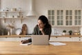 Confident woman using laptop, taking notes, sitting in kitchen