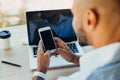 Confident young african american businessman working on laptop and talking on a cell phone while sitting at his workplace in Royalty Free Stock Photo