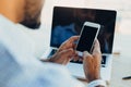 Confident young african american businessman working on laptop and talking on a cell phone while sitting at his workplace in Royalty Free Stock Photo