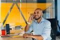 Have a nice working day. Confident young african american businessman working on laptop and talking on cell phone while sitting at Royalty Free Stock Photo