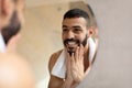 Confident young Arab guy looking in the mirror, touching beard