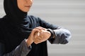 Confident young arab lady athlete in hijab checks pulse on fitness tracker on wall background, cropped, close up