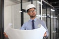 Confident young architect in hardhat holding a blueprint and looking at area for work Royalty Free Stock Photo