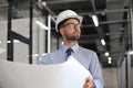 Confident young architect in hardhat holding a blueprint and looking at area for work Royalty Free Stock Photo