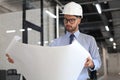 Confident young architect in hardhat holding a blueprint and looking at it Royalty Free Stock Photo