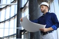 Confident young architect in navy shirt and hardhat holding a blueprint and looking at it Royalty Free Stock Photo
