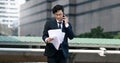 Confident young Asian business man in suit analyzing charts or paperwork in hands outdoors