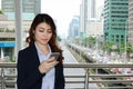 Confident young Asian business woman looking mobile smart phone in her hands at urban building city background. Royalty Free Stock Photo