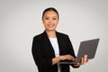 A confident young Asian businesswoman in a black blazer and white top holds an open laptop Royalty Free Stock Photo