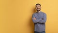 Confident young asian man standing with folded arms over yellow background Royalty Free Stock Photo