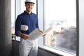 Confident young business man in hardhat holding blueprint and looking away while standing indoors Royalty Free Stock Photo