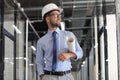 Confident young business man in hardhat holding blueprint and looking away while standing indoors Royalty Free Stock Photo